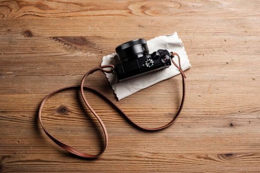 vintage style of digital mirrorless camera with leather strap isolated on wooden background