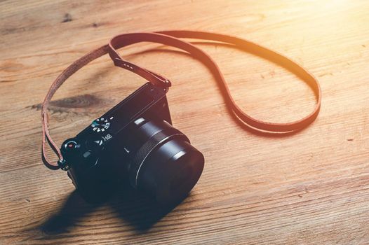 vintage style of digital mirrorless camera with leather strap isolated on wooden background