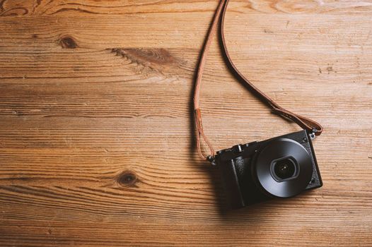 vintage style of digital mirrorless camera with leather strap isolated on wooden background