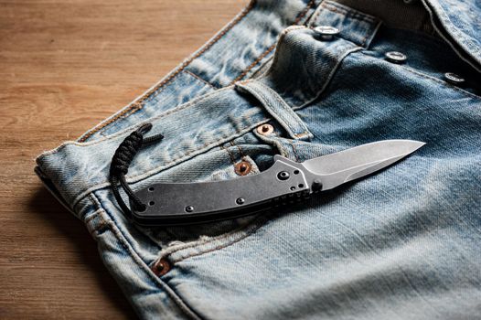 folding knife and jeans. closeup stainless steel pocketknife with blackwash finish on blade and handle.