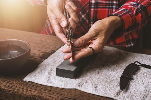 The man using whetstone to sharpening his pocket knife. Pocket knife care and maintenance concept.