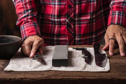 The man using whetstone to sharpening his pocket knife. Pocket knife care and maintenance concept.