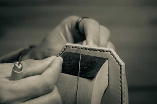 Sewing the vegetable tanned leather by hand. Leather and the craft tools. Monotone and shallow depth of field.