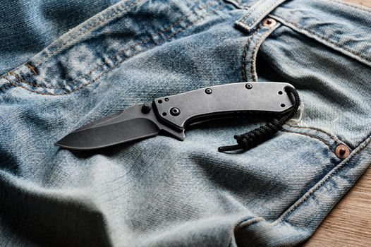 folding knife and jeans. closeup stainless steel pocketknife with blackwash finish on blade and handle.