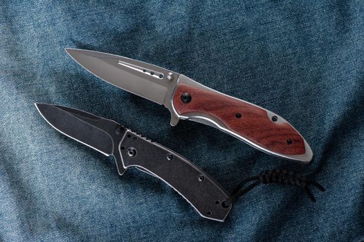 two stainless steel folding knifes over denim jacket