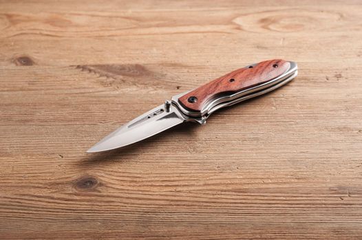 stainless steel folding knife isolated over wood background