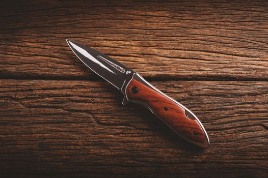 stainless steel folding knife isolated over wood background