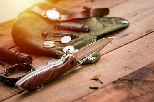 many men's items on wood plank, closeup at stainless steel folding knife.