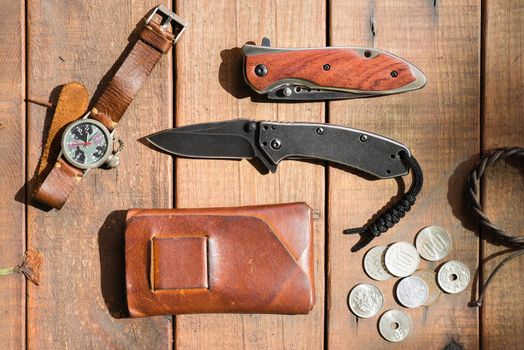 many men's items on wood plank, closeup at stainless steel folding knife.