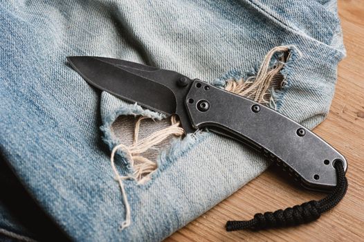 folding knife and jeans. closeup stainless steel pocketknife with blackwash finish on blade and handle.