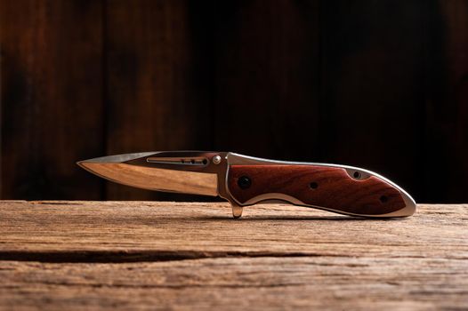 stainless steel folding knife isolated over wood background