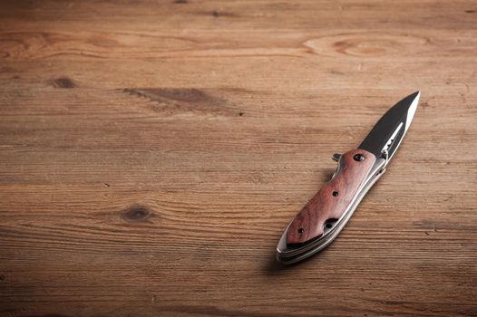 stainless steel folding knife isolated over wood background