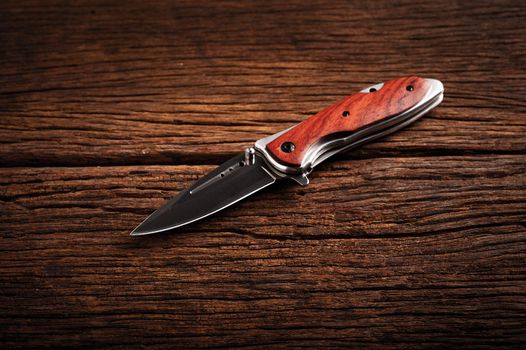 stainless steel folding knife isolated over wood background