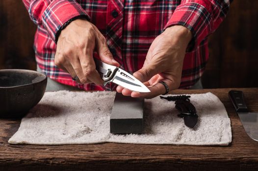 The man using whetstone to sharpening his pocket knife. Pocket knife care and maintenance concept.