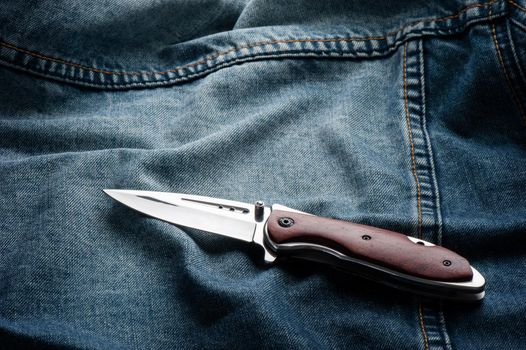 stainless steel folding knife with wooden handle isolated on Jeans.
