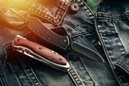 two stainless steel folding knifes over denim jacket