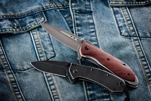 two stainless steel folding knifes over denim jacket