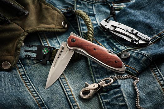 stainless steel folding knife and other everyday carry (EDC) items for men. closeup at folding knife. (low light and shallow depth of field)