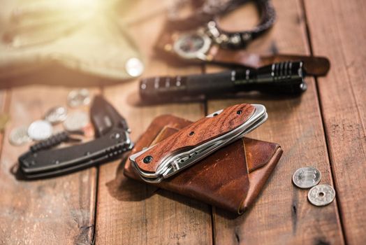 many men's items on wood plank, closeup at stainless steel folding knife.