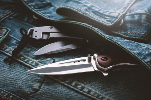 two stainless steel folding knifes over denim jacket