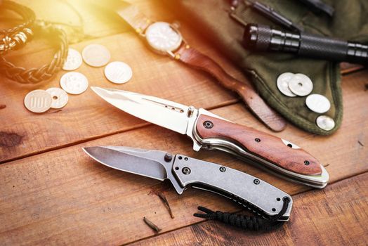 many men's items on wood plank, closeup at stainless steel folding knife.