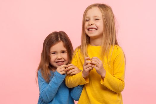 Two funny naughty little girls cunningly looking at camera and plotting tricky plan together, scheming excellent idea to prank friend, bad behavior. indoor studio shot isolated on pink background
