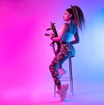 a cheeky girl with braided dreadlocks on her head in neon light with an automatic rifle in neon light