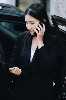 Asian businessmen, business owners, company presidents or female employees talking on the phone and holding a tablet are getting out of the car to attend a business plan meeting at the meeting