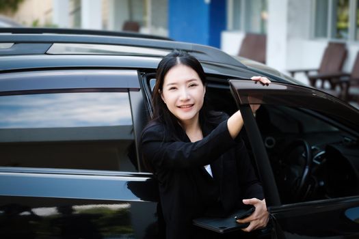 Asian businessmen, business owners, company presidents or female employees holding smartphone mobile and a tablet are getting out of the car to attend a business plan meeting at the meeting