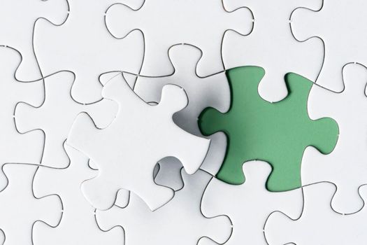 White jigsaw puzzle with missing piece on green background. Copy space. Flat lay. Directly above.