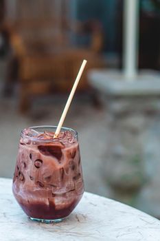 Close up of a glass of Iced Cocoa cool drink served on table. Iced chocolate drink in classic glass on green nature of summer background. Summer drink