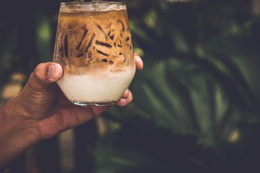 Selective focus Hand Hold Glass of iced coffee on dark summer nature background