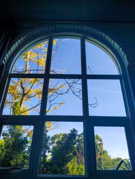 Arched window with view to autumnal landscape, bright sunshine. View through the window in autumn.