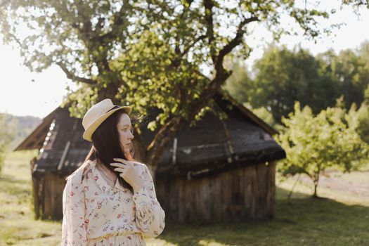 romantic portrait of a young woman in straw hat and beautiful dress in the countryside in summer.