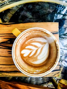 Close up cup of art of a cappuccino leaf design coffee mug on wooden plate