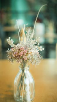 Bunch of dried flowers in a glass vase on wooden table.