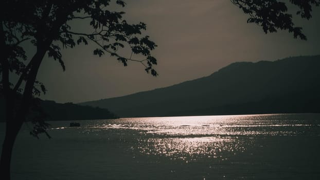 light reflection by surface waves of a lake at sunset with mountain background.