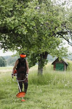 Worker man mowing tall grass with petrol lawn trimmer in the garden or backyard. Process of lawn trimming