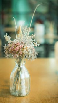 Bunch of dried flowers in a glass vase on wooden table.