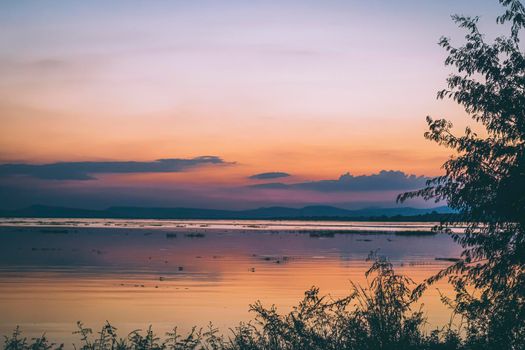 long exposure vanilla colorful sky and  lake reflection with mountains in the background. blurred wild grass blowing in the wind on foreground