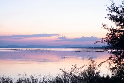 long exposure vanilla colorful sky and  lake reflection with mountains in the background. blurred wild grass blowing in the wind on foreground