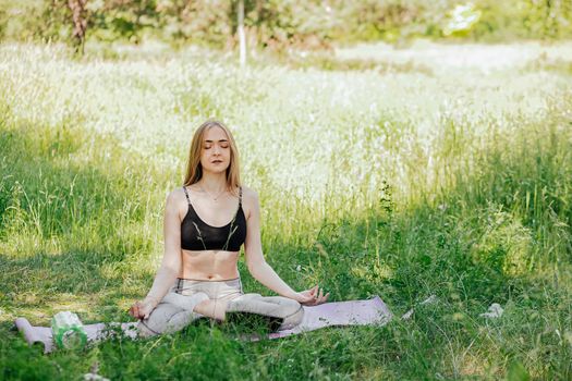 Yoga woman on green grass girl relaxes in the field. Yoga woman in green park girl doing gymnastics outdoors. Meditating woman in meditation in yoga pose practices outdoors