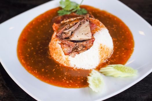 Red barbecued pork on rice, food serve with sweet curry and vegetable (cucumber, coriander) on white ceramic plate.