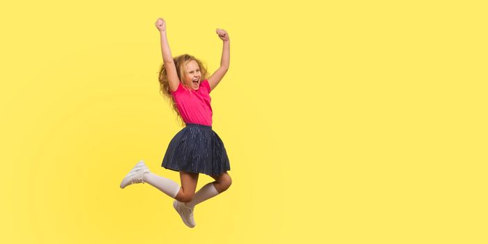 I am champion. Full length portrait of ambitious little girl in dress jumping in air and shouting from happiness, inspired child celebrating success. indoor studio shot isolated on yellow background