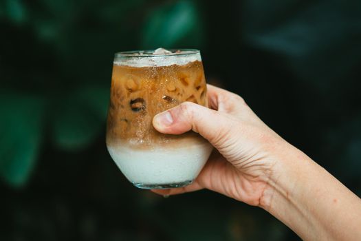 Hand hold iced latte coffee in a glass with cream on bottom . cold summer drink background