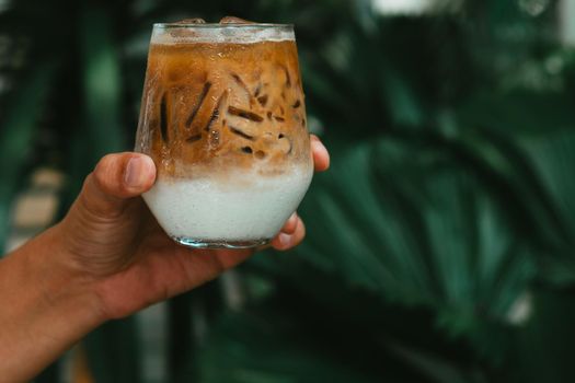 Hand hold iced latte coffee in a glass with cream on bottom . cold summer drink background