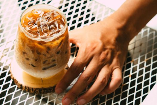 Hand hold iced latte coffee in a glass with cream on bottom . cold summer drink background
