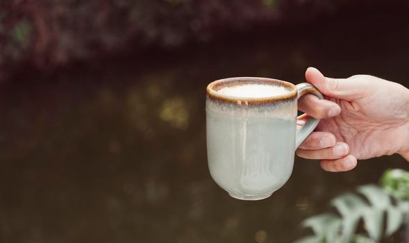 Hands of a man or barista holding cup of hot coffee latte with heart shaped foam art