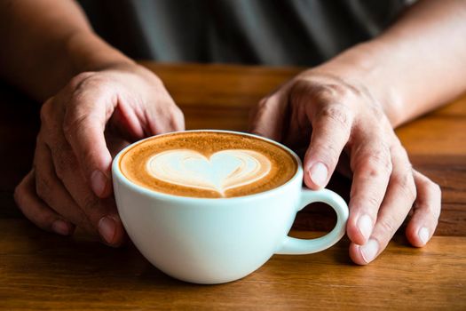 Hands of a man or barista holding cup of hot coffee latte with heart shaped foam art