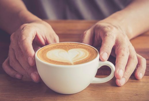 Hands of a man or barista holding cup of hot coffee latte with heart shaped foam art